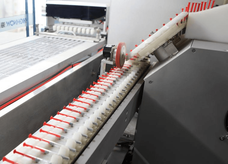Inclined chute and linear feeder handling pre-filled syringes gently on a blister cartoning machine