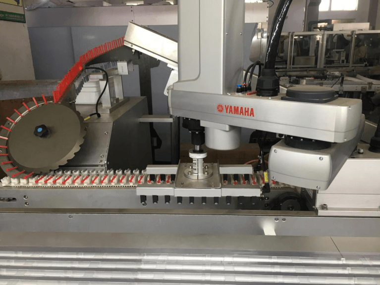 Robotic loading station with rotary star-wheel sorting feeder placing pre-filled syringes into blister trays